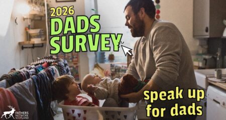 Picture of a father caring for two young children in a kitchen. One older child is sitting in a laundry basket whilst the father places the younger child, a baby, in the basket next to him. Laundry can be seen drying in the background. There is accompanying text which says '2026 Dads Survey' and 'speak up for dads'